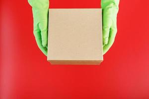 The parcel from the delivery service in the hands with green rubber gloves on a red background. photo