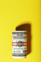un rollo de billetes americanos de cien dólares está atado con una banda elástica roja sobre un fondo amarillo. foto