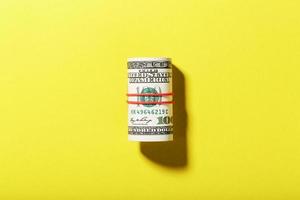 A roll of hundred-dollar American bills is tied with a red elastic band on a yellow background. photo