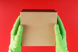 el paquete del servicio de entrega en las manos con guantes de goma verdes sobre un fondo rojo. foto