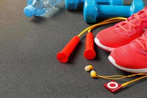 Top view of sports equipment, dumbbells, a skipping rope, a bottle of water, sneakers and a player. Isolated on a gray photo