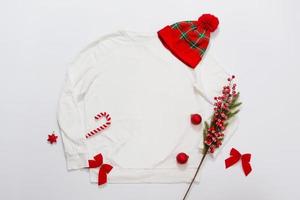Close up white blank template sweatshirt copy space. Christmas Holiday concept. Top view mockup sweatshirt, hat. Red holidays decorations on white background. Happy New Year accessories. Xmas outfit photo