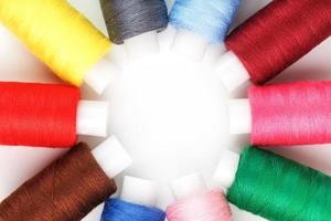hilos de coser de diferentes colores en carretes sobre un fondo blanco en un círculo. foto