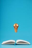 A gold-colored light bulb hangs above the blank pages of a notebook on a blue background. photo