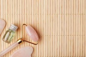 Gua sha massage made of natural rose Quartz-roller, jade stone and oil, on a bamboo background for face and body care. photo
