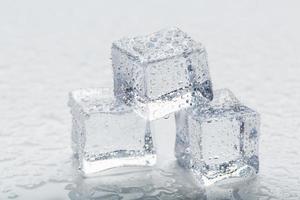 cubos de hielo en forma de pirámide con gotas de agua cerca - en macro sobre un fondo blanco. foto