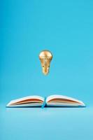 A gold-colored light bulb hangs above the blank pages of a notebook on a blue background. photo