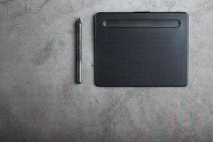 Graphic tablet with a stylus on a dark textural background, top view. Gadget for working as a designer, artist and photographer photo