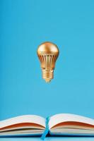 A gold-colored light bulb hangs above the blank pages of a notebook on a blue background. photo