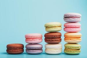 Macaroni cookies of different colors are arranged in the shape of pyramid steps on a blue background. photo