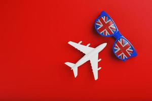 White airplane and sunglasses with the flag of the United Kingdom on a red background. Travel to England. photo