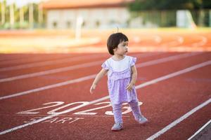 el bebé asiático comienza a correr en el nuevo año 2023. el inicio de la niña corredora corriendo en la pista de carreras de carril de entrenamiento va a la meta del éxito. personas corriendo como parte del número 2023. cuidado de la salud deportiva. foto