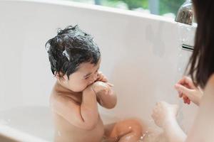 Asian cute kid girl toddler having a bath wash hair cleaning bathing bath tub with her mother. Mother love and care happy baby girl  innocent have fun playing with water enjoying. Baby concept. photo