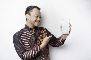 un retrato de un hombre asiático sonriente que lleva un pantalones de batik y muestra una pantalla verde en su teléfono, aislado de fondo blanco foto