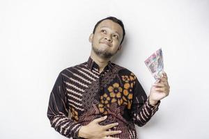 Photo of a hungry excited young Asian man holding money in Indonesian Rupiah and wondering what to order yummy food isolated on white color background