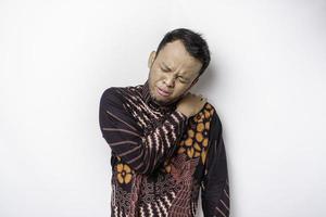 Tired upset young man wears batik shirt suffering from pain, muscle spasm at workplace. Fatigue, deadline, pain and incorrect posture photo