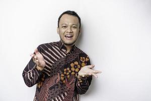 Young Asian man wearing batik shirt standing over isolated white background pointing fingers to camera with happy face. Good energy and vibes. photo