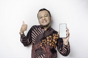 un retrato de un hombre asiático sonriente que lleva un pantalones de batik y muestra una pantalla verde en su teléfono, aislado de fondo blanco foto