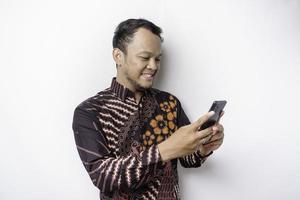 A portrait of a happy Asian man wearing batik shirt and holding his phone, isolated by white background photo