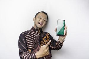 un retrato de un hombre asiático sonriente que lleva un pantalones de batik y muestra una pantalla verde en su teléfono, aislado de fondo blanco foto