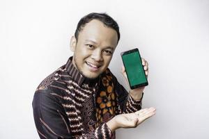 A portrait of a smiling Asian man wearing a batik shirt and showing green screen on her phone, isolated by white background photo