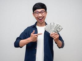 un hombre asiático positivo sonríe y señala con el dedo un montón de dinero en la mano foto