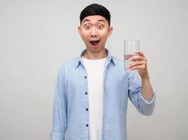 Young positive man blue shirt hold glass of water feels amazed isolated photo