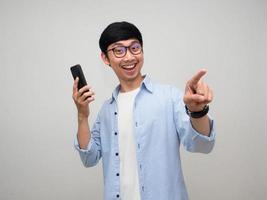 Positive asian man holding mobile phone smile posing point finger isolated photo
