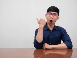 un hombre de negocios asiático positivo usa un gesto de anteojos asombrado y apunta con el dedo al espacio de la copia foto