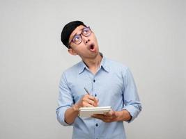 Young businessman writing on notebook gesture looking up isolated photo