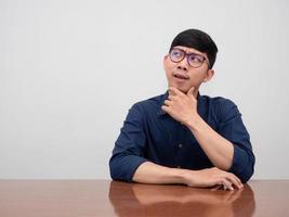 Asian businessman wear glasses sit at the table thoughtful gesture looking at copy space photo