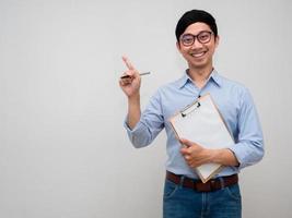 Positive asian businessman wear glasses hold document board posing point finger isolated photo