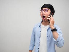 Young asian man glasses hold mobile phone feels amazed isolated photo