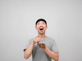 Asian man grey shirt press finger at smart phone feels excited gesture looking up isolated photo