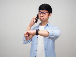 Young businessman hold mobile phone and looking at his watch isolated photo