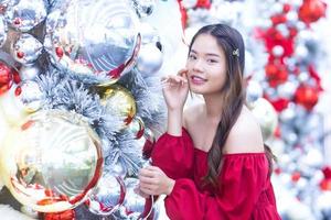 Beautiful Asian woman wears red coat while looks at camera smiling happily in Christmas and New Year celebration theme on bokeh background. photo