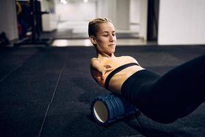 Armless athlete massaging her back with foam roller after exercising in a gym. photo