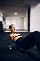 mujer atlética con discapacidad física usando rodillo de espuma mientras se calienta para entrenamiento deportivo en un gimnasio. foto