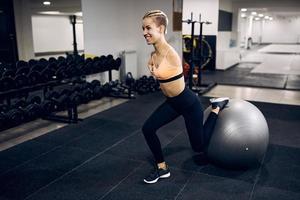mujer atlética feliz sin las extremidades superiores usando pelota de fitness mientras hace ejercicio en un gimnasio. foto
