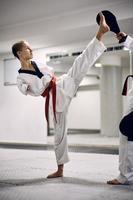 artista marcial con para-habilidad ejerciendo una patada alta con su compañero ahorrador durante el entrenamiento de taekwondo en el club de salud. foto