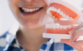 Stomatology concept, partial portrait of girl with strong white teeth looking at camera and smiling, fingers near face. Closeup of young woman at dentist's, studio, indoors photo