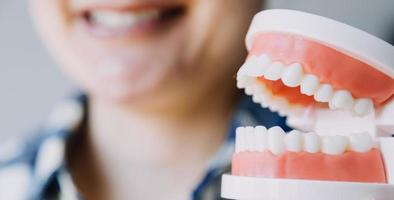 concepto de estomatología, retrato parcial de una chica con fuertes dientes blancos mirando la cámara y sonriendo, con los dedos cerca de la cara. primer plano, de, mujer joven, en, dentista, estudio, adentro foto