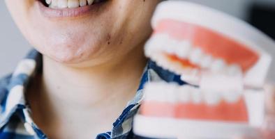 concepto de estomatología, retrato parcial de una chica con fuertes dientes blancos mirando la cámara y sonriendo, con los dedos cerca de la cara. primer plano, de, mujer joven, en, dentista, estudio, adentro foto