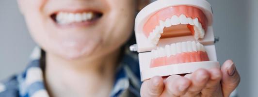 concepto de estomatología, retrato parcial de una chica con fuertes dientes blancos mirando la cámara y sonriendo, con los dedos cerca de la cara. primer plano, de, mujer joven, en, dentista, estudio, adentro foto