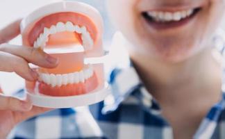 concepto de estomatología, retrato parcial de una chica con fuertes dientes blancos mirando la cámara y sonriendo, con los dedos cerca de la cara. primer plano, de, mujer joven, en, dentista, estudio, adentro foto