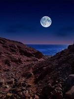 vista panorámica del mar rojo por la noche con luna llena sobre el mar y las montañas foto