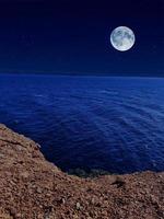 vista panorámica del mar rojo por la noche con luna llena sobre el mar y las montañas foto