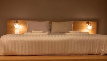 almohadas blancas y mantas en la cama con luz de lámparas por la noche foto