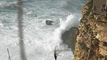 die schönen wellen, die am felsigen bergufer von nazare, portugal, krachen und spritzen - zeitlupe video