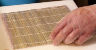 Chef Puts Seaweed Wrap And Sushi Rice On A Bamboo Mat For Rolling - close up, slow motion video